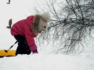A girl climbs a mountain in the snow on the descent to ride rubber tubes. Clear frosty winter day.