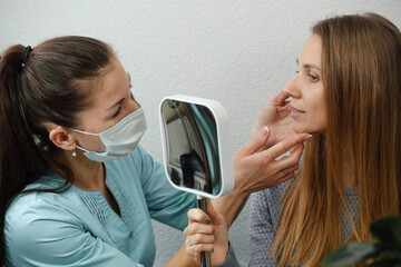Client checking with dermatology cosmetician specialist with mirror, discussion skin face problems...