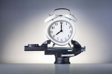 Alarm clock squeezed in a vise on grey background. Time Pressure concept.