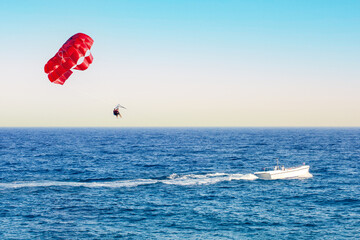 Red parasail wing pulled by a boat.  Positive human emotions, feelings, family, travel, vacation.