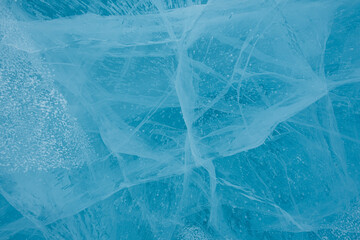 Texture of beautiful blue ice with cracks and air bubbles in the frozen lake. Winter nature background. 