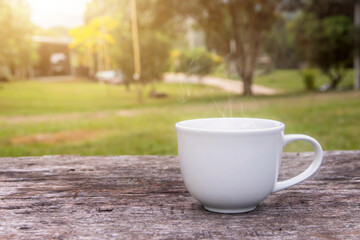 A white cup of hot espresso coffee mugs placed on a wooden floor with morning fog and moutains with sunlight background,coffee morning