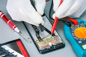 Repairing smartphone with multimeter in lab. Checking damaged mobile phone with digital multimeter.