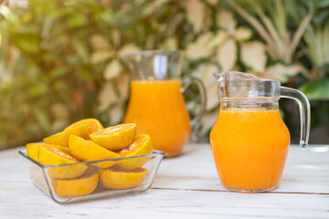 Fresh orange slices with jar of orange juice on wooden table with garden tree background.