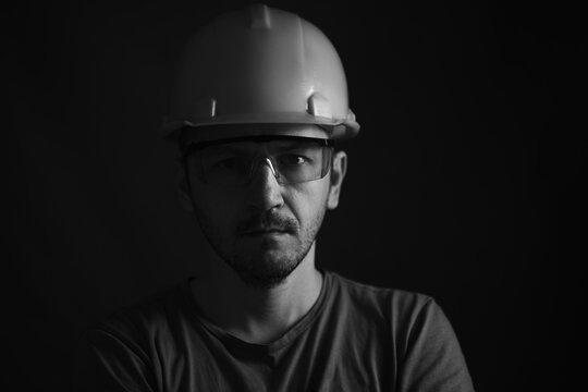 Miner face on black background. Head tired miner in helmet and glasses. Black and white photographic portrait.