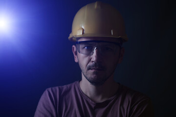Miner face on black background. Head tired miner in helmet and glasses.Bright blue light from...