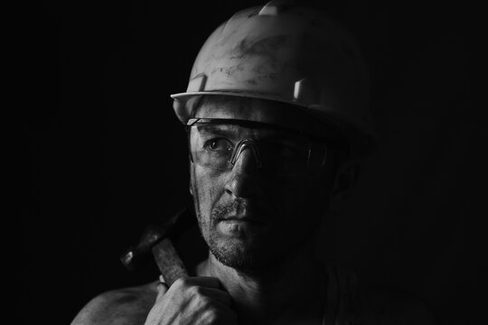 Miner face on black background. Head tired miner in helmet and glasses. Black and white photographic portrait.