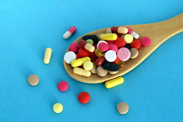 On a wooden spoon lie pills and capsules of different colors on a blue background.