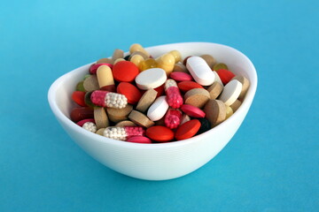 A small white plate contains many pills and capsules of different colors.