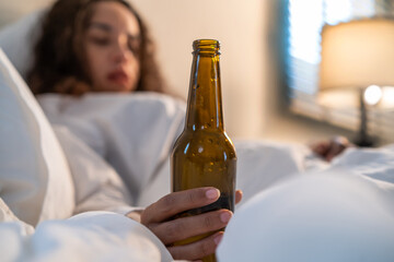 Drunk Latino woman hold beer bottle, and crying feel hangover on bed. 