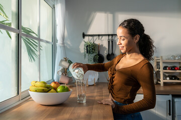Young beautiful Latino woman pouring clean water into glass in kitchen