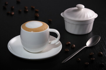 Cappuccino on a dark table. Breakfast coffee on a black background. White cup of coffee on a black textured table. Cup of coffee on a black background. Coffee beans on black slate.