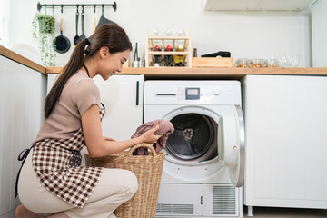 Asian beautiful woman put dirty clothes to washing machine in house.