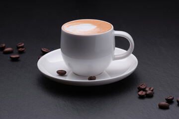 White cup of coffee with coffee beans on a black background side view. Coffee with milk on a black background close up.