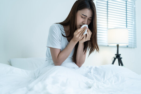 Asian sick girl in pajamas wake up from sleep at night sneezing on bed