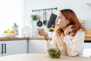 Asian young happy attractive woman eat green salad in kitchen at home. 