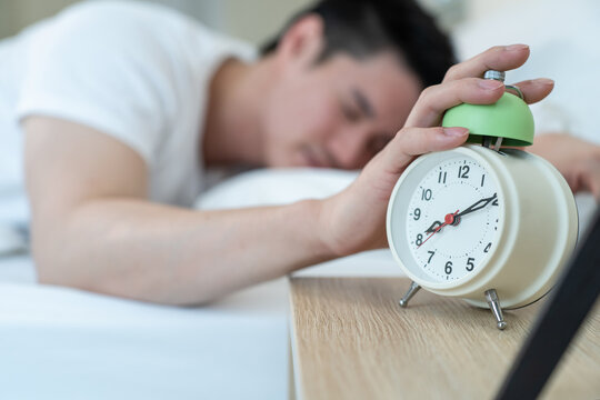 Asian attractive young man turn off alarm clock ringing in the morning