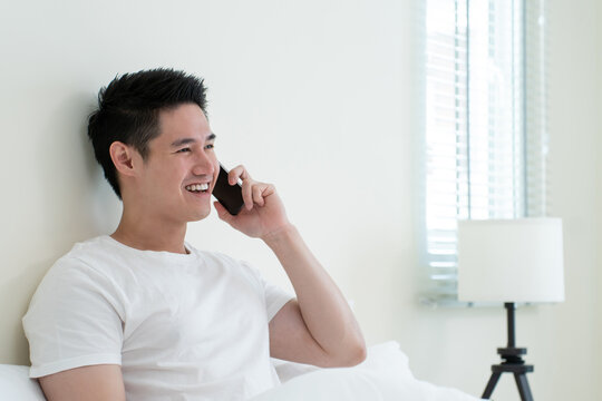 Asian handsome man talk on mobile phone call on bed at home in morning