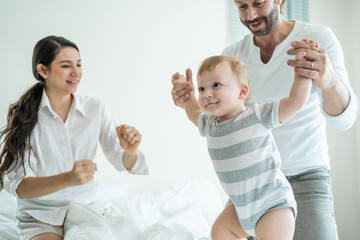 Caucasian loving parents play with baby boy child on bed in bedroom. 
