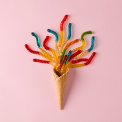 Ice cream cone with gummy candies on pink background.