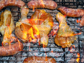 Chicken legs and meat sausages on an iron barbecue net over the fire. Cooking over a fire. Grill mesh. Chicken and meat sausages. Healthy eating. Food in nature. Menu of dishes. Background image.