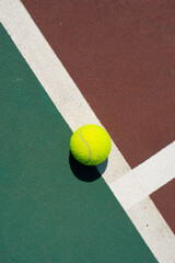 Yellow tennis ball lying on line of the red and green court. Flat lay view. Space for text