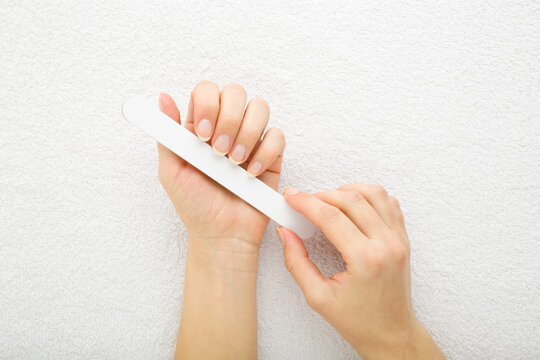 Young adult woman hand using nail file and filing nails on white towel background. Closeup. Point of view shot. Care about fingernails. Top down view.