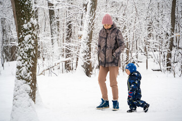 Little preschooler kid walks with his mother in the winter forest.