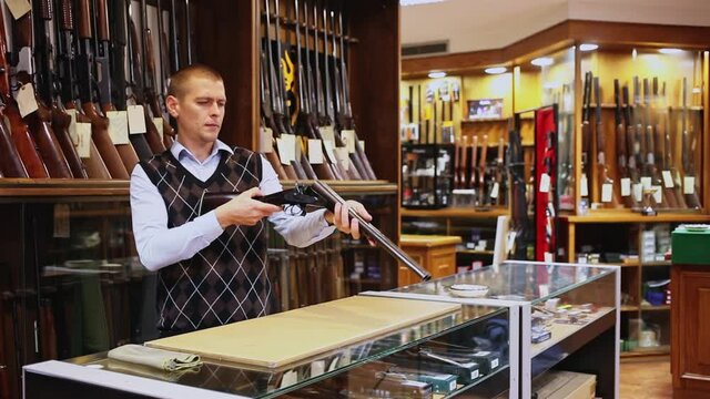 Salesman standing behind counter at gun shop, showing double barreled hunting rifle . High quality FullHD footage