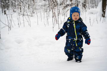 Fototapeta na wymiar A joyful and independent kid walks through the winter forest.