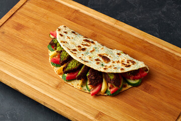 tortilla with falafel, cucumber and tomato on a wooden board