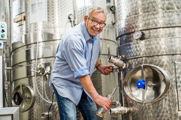 Technician filling wine from storage tank in winery. Wine industry concept.