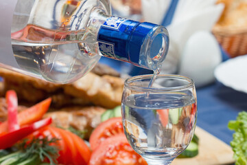 Close-up of a waiter pours vodka into a customer's glass.
