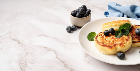 Cottage cheese pancakes served with curd and blueberries, high angle view on marble background, copy space