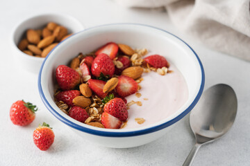 Strawberry yogurt with fresh berries, homemade granola, almonds in bowl. Healthy breakfast on light background
