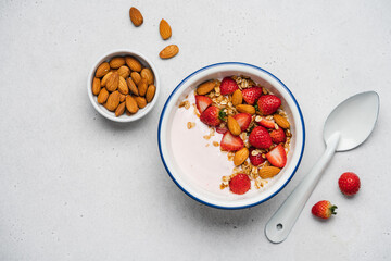 Strawberry yogurt with fresh berries, homemade granola, almonds in bowl. Healthy breakfast on light background