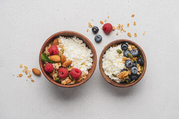 Fototapeta premium Two different Cottage cheese bowl with blueberries and raspberries, granola, almonds, walnuts and honey. Servings of healthy breakfast on light gray background