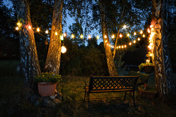 string of lights in the garden with garden bench and sheltered corner hidden by hedges in the...
