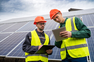 two strong skilled men in helmets and vests stand and talk in solar panels.