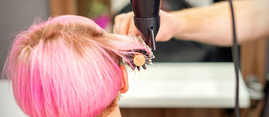 Naklejka premium A professional hairdresser is drying long red hair with a hair dryer and round brush, close up