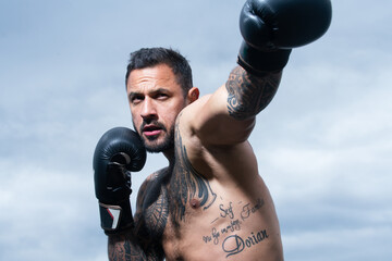 Boxer in a fight. Fist fight. Strong man with tattooed body boxing outdoor. Man with muscular body...
