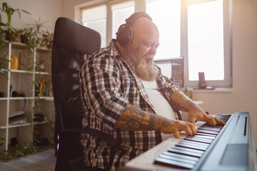 Emotional plump man composer writes music playing sound synthesizer in studio