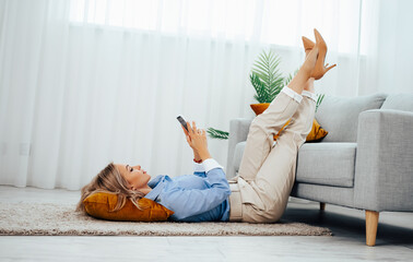 Lazy leisure, girl with a phone in her hand lying on the floor near the sofa raising her legs up....