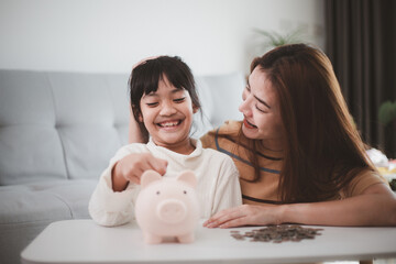 Mother and daughter putting coins into piggy bank. Family budget and savings concept. Junior...