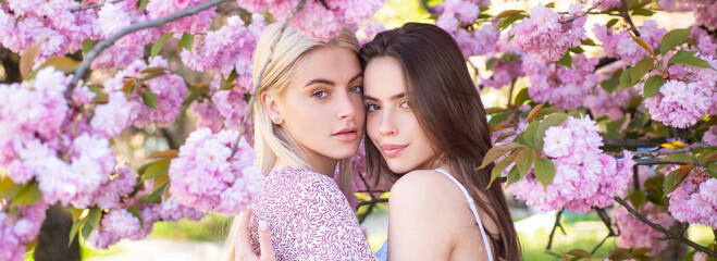 Spring banner with women girlfriends outdoor. Two young sensual sexy women relaxing in sakura flowers.