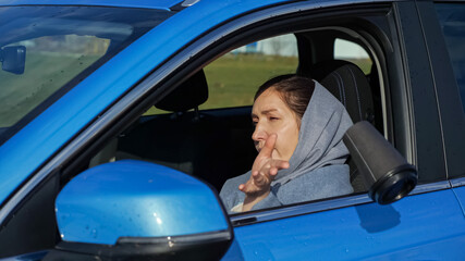 Fototapeta na wymiar Woman wrapped in warm scarf with brunette hair finishes drinking hot coffee and throws plastic cup away out of car window on autumn street, side view
