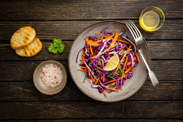 Fresh coleslaw salad made of shredded red and white cabbage and carrots on dark wooden background, top view
