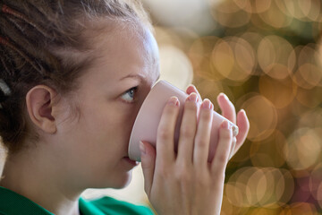 On christmas eve young woman with dreadlocks drinks coffee inside.