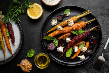 Roasted young whole colorful carrot with herbs and cheese served on plate over black background. Top view
