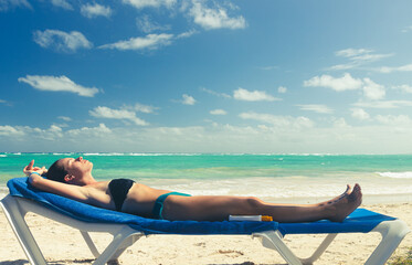 A beautiful adult woman wearing a swimsuit lies down on the ocean beach and sunbathes. Getting away from it all.
